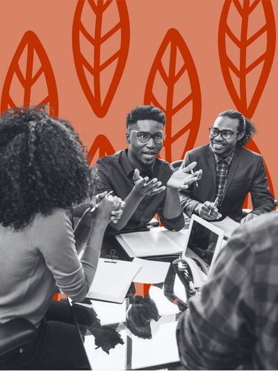 A black and white image of a group of four dark skin young people talking with each other while sitting at a table with notebooks and a laptop open.